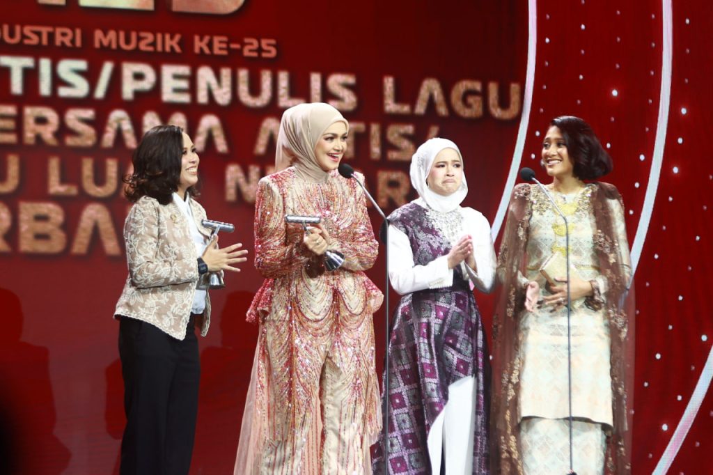 Datuk Seri Siti Nurhaliza tersenyum di pentas AIM25 memegang trofi bersama barisan artis dan penyampai anugerah