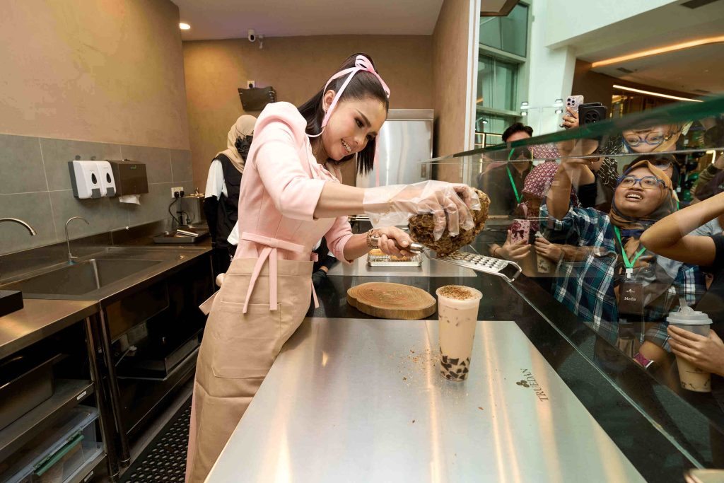 Actress Bella Astillah wearing an apron while grating brown sugar behind the beverage counter at TRUEDAN Malaysia launch
