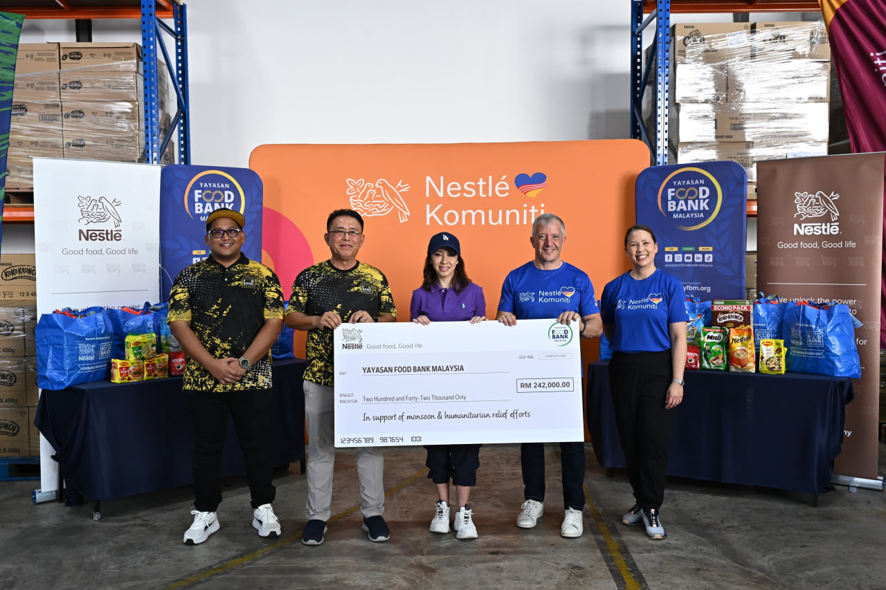 Wakil Nestlé Malaysia dan Yayasan Food Bank Malaysia memegang replika cek RM242,000 di hadapan timbunan kotak makanan